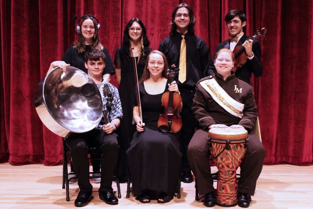 Pictured from left seated: Kaleb Humes, Trixie Calissie and Olivia Miller. Standing from left: Trishtan Markey, Sydney Coss, Issac Perry and Chris Evans. They are seated or standing in front of a red curtain. 