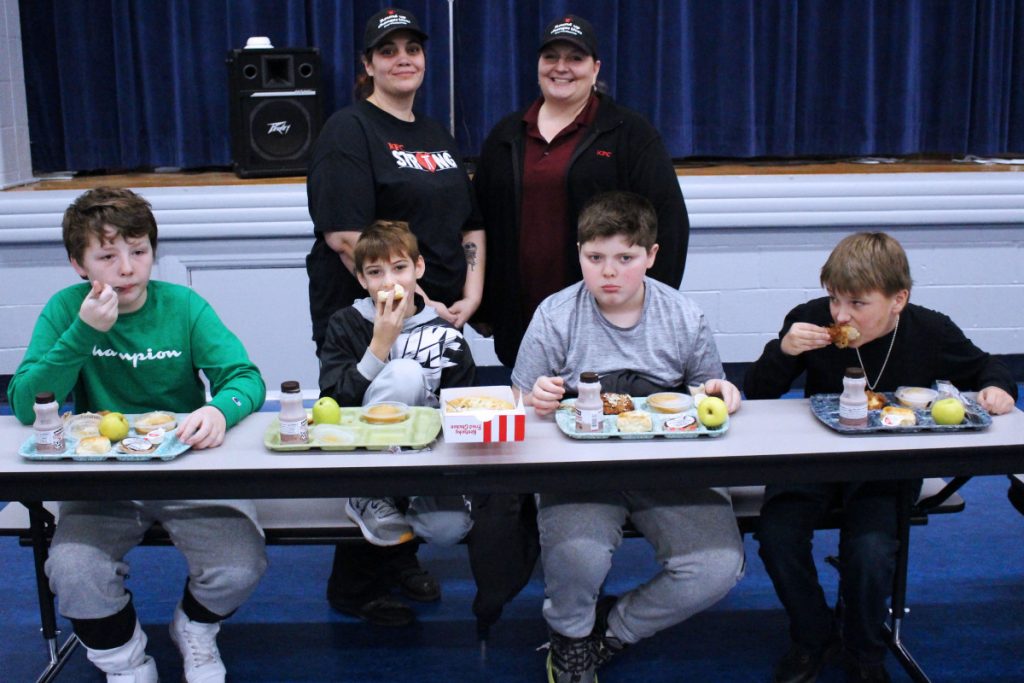 Seated from left: Central Elementary fourth grade students Rion Wolfe, Ryder Wilson, Damon Wyatt and Erick Virden eat the meal KFC served to them Tuesday. Standing from left: KFC employee Brittany Wilson and Moundsville KFC General Manager Patricia Robinson enjoy watching the students at lunch.