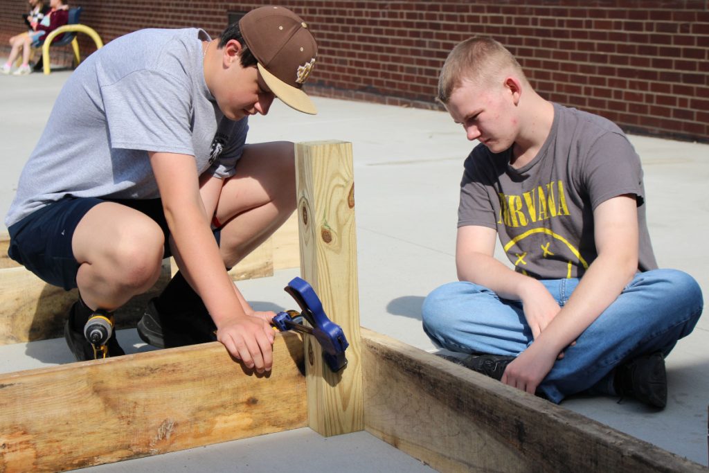 two students secure the corners of the raised garden bed to a 2 by 4 leg.