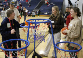 Special Olympics athlete Nathan slam dunks a basketball while peer tutors cheer for him.