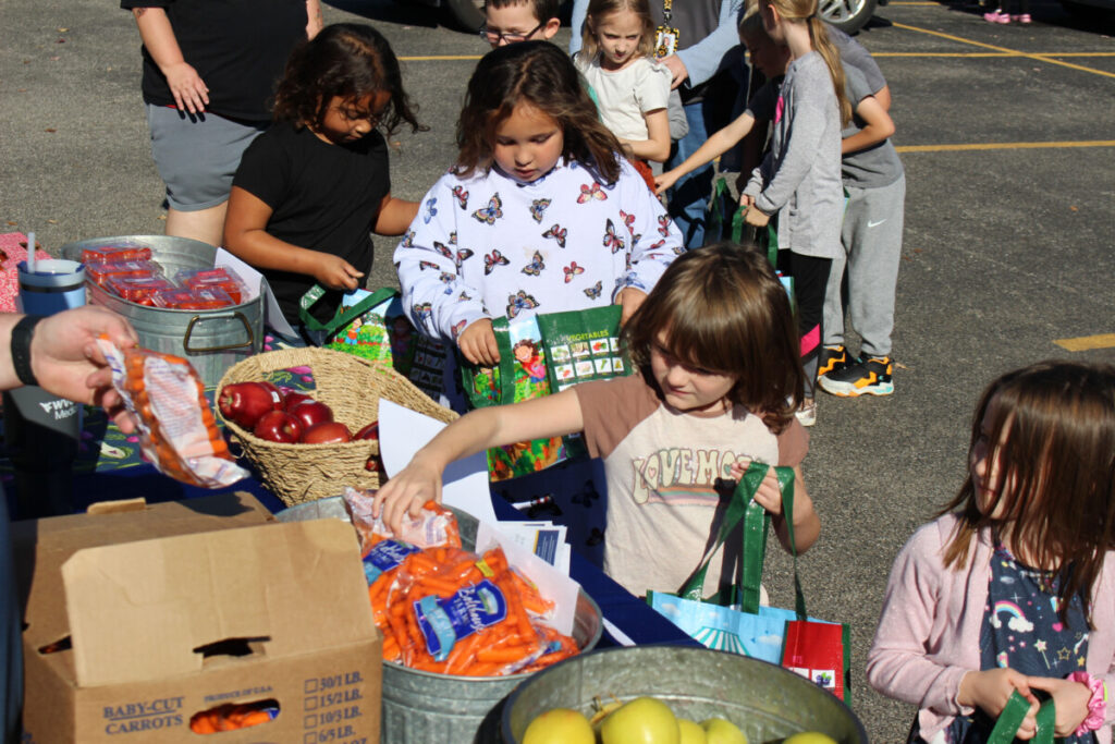 Kids pick out fruits and vegetables to put in their shopping bags.