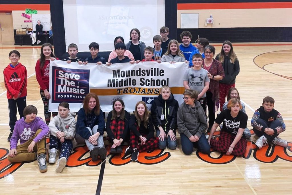 Group of Moundsville Middle School students in the gym holding a VH1 VH1 Save the Music Foundation banner.
