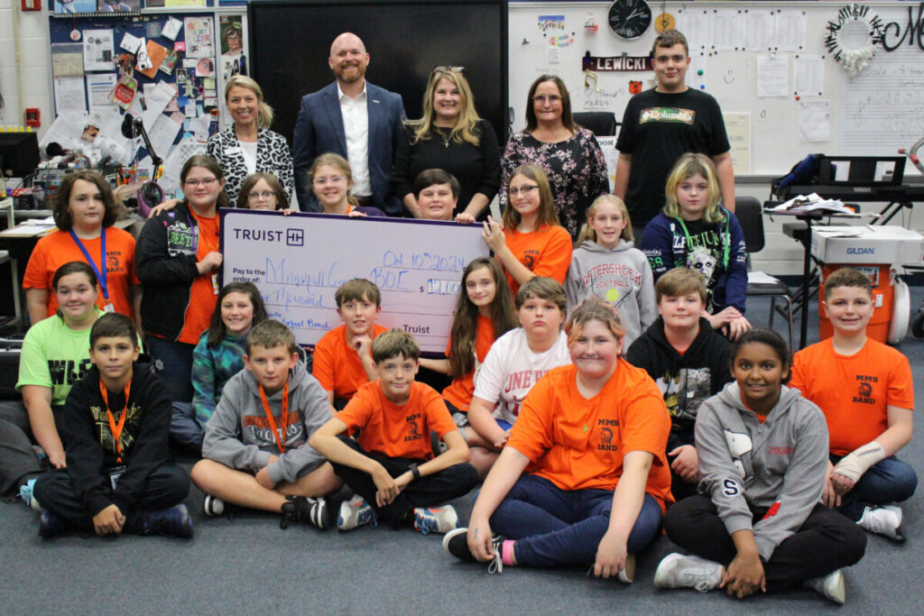 Members of the Evan G. Roberts Trust committee are presenting Sue Lewicki and her band students with an oversized check.