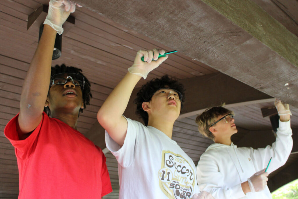 Pictured from left: MMS students A.V. Jackson, Kingsley Zheng and Dominic Kennen pull out staples and thumbtacks left over from removed party decorations at a Grand Vue picnic shelter. 