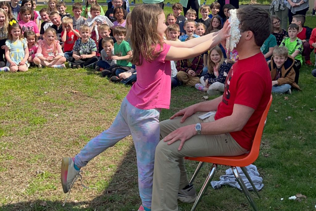 A student pushes a pie into a teacher's face.